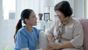 An elderly woman chats with a staff member in a bright, comfortable living area.
