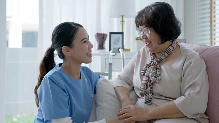An elderly woman chats with a staff member in a bright, comfortable living area.